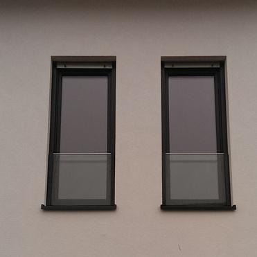 Zwei senkrechte Fenster mit schwarzem Rahmen, oberhalb einer großen Glasfront an einer weißen Hauswand.