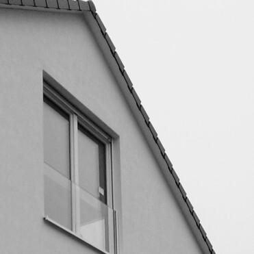 Detailansicht eines modernen Hauses mit einer schrägen Dachlinie und zwei Fenstern, in Schwarzweiß.
