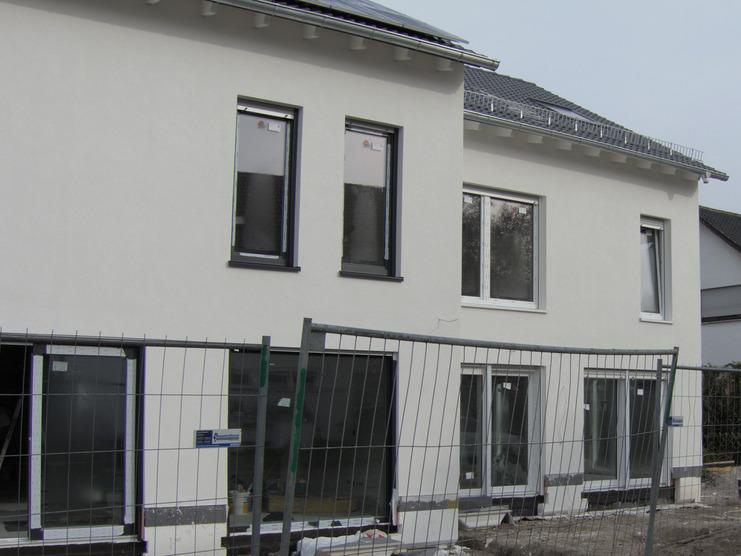 Neubau eines weißen Hauses mit Baustellenzaun und unbefestigtem Boden an einer Straße.