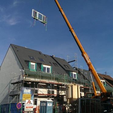 Kran hebt ein Fenster zur Installation an einem mehrstöckigen Gebäude mit Gerüst und blauer Himmel im Hintergrund.