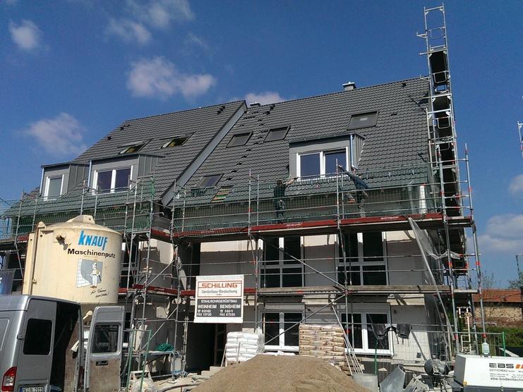 Bau eines Mehrfamilienhauses mit Gerüst, noch nicht vollständig gedecktem Dach und Baustellenfahrzeugen im Vordergrund.
