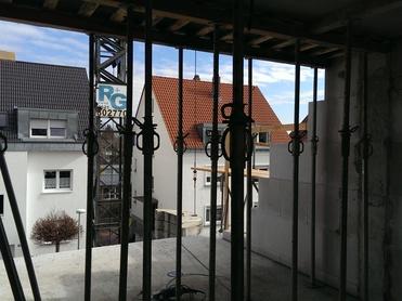 Blick durch ein Gerüst auf angrenzende Häuser mit unterschiedlichen Dächern und einem Kran im Hintergrund.