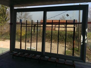 Blick durch einen offenen Fensterrahmen auf eine Baustelle mit Arbeiter und unbefestigten Fenstern im Hintergrund.