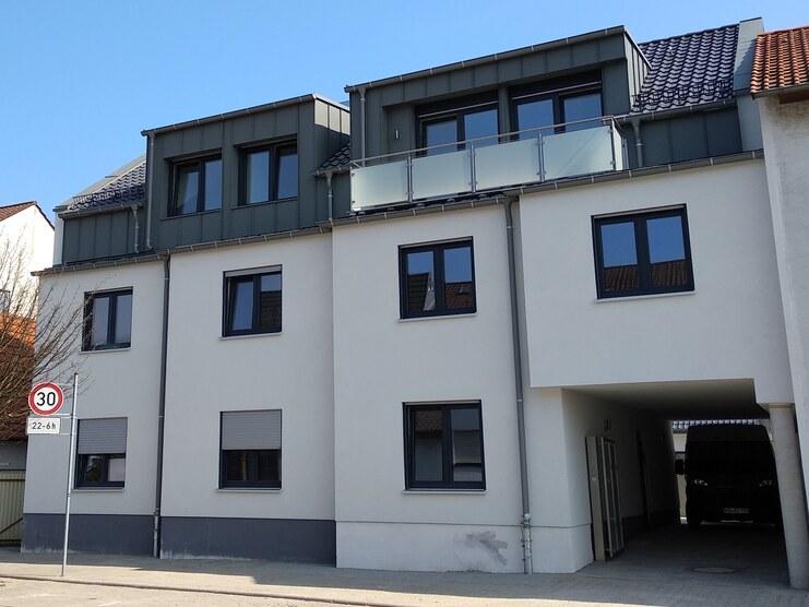 Moderne Wohnanlage mit flachdachigem Obergeschoss und Balkon, an einer Stadtstraße mit Nachbarhäusern.
