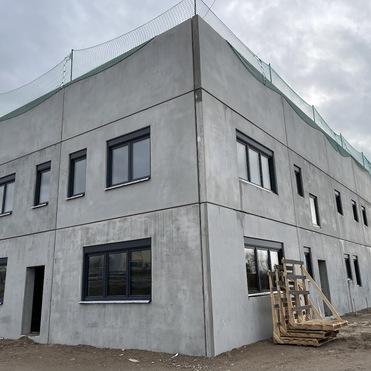Baustelle eines modernen Gebäudes mit Betonwänden und Fenstern, umgeben von Baugeräten und Netz zum Arbeitsschutz.