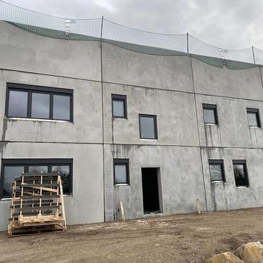 Fassade eines unvollendeten Gebäudes mit Fenster und einem Holzstapel im Vordergrund.