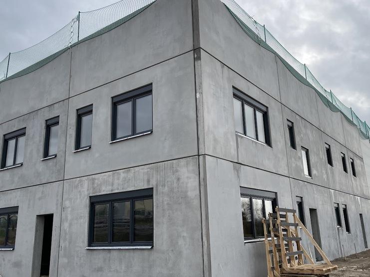 Baustelle eines modernen Gebäudes mit Betonwänden und Fenstern, umgeben von Baugeräten und Netz zum Arbeitsschutz.