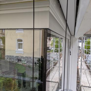 Blick auf eine Fenstersituation mit reflektierenden Glasflächen und Baugerüst im Hintergrund.
