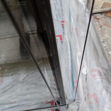 Blick auf einen Gebäudeeingang mit transparenten Glaswänden und Schutzfolie am Boden während der Bauarbeiten.