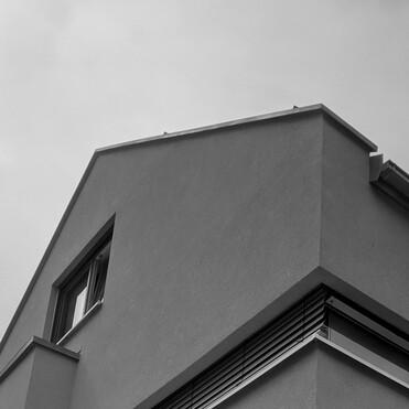 Detailaufnahme einer Hausecke mit Fenster und schrägem Dach in Schwarzweiß.