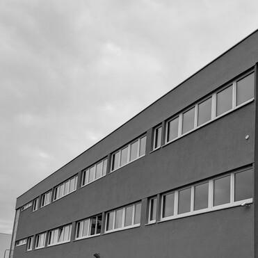 Schlichte graue Gebäudeansicht mit mehreren Fenstern unter einem bewölkten Himmel.