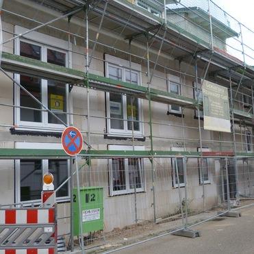 Fassade eines Gebäudes mit Gerüst und Fensteröffnungen, auf einer Straße ohne Parkmöglichkeiten.