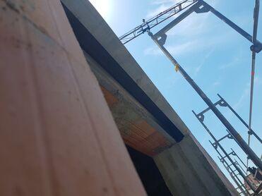 Blick auf eine Baustelle mit einem Kran und Betonstruktur unter blauem Himmel.
