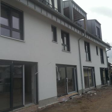 Fassade eines neugebauten Mehrfamilienhauses mit Fenster und Balkonen, umgeben von Baustellenmaterial.