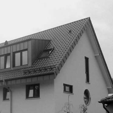 Dachansicht eines modernen, weiß gestrichenen Hauses mit schrägem Dach und Dachfenstern in Schwarz-Weiß.