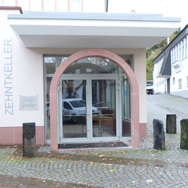 Eingang des Zehntkellers mit gl&auml;serner T&uuml;r und runder Abdeckung, umgeben von einer gepflasterten Stra&szlig;e.