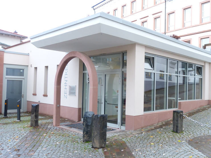 Fassade eines modernen Geb&auml;udes mit Glasfront und geschwungener Eingangst&uuml;r, in einer gepflasterten Stra&szlig;e.