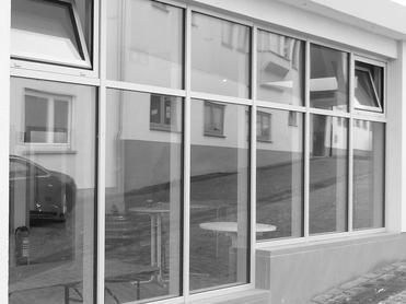Fensterfront eines Gebäudes mit Spiegelungen einer Straße und Tischen im Außenbereich.