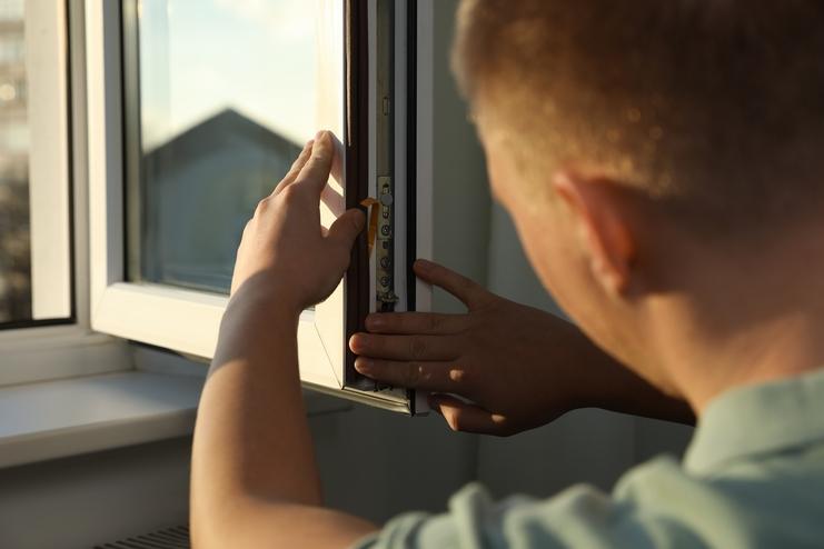 Mann montiert ein Fenster, während er sorgfältig den Rahmen und die Mechanik justiert. Tageslicht strömt herein.