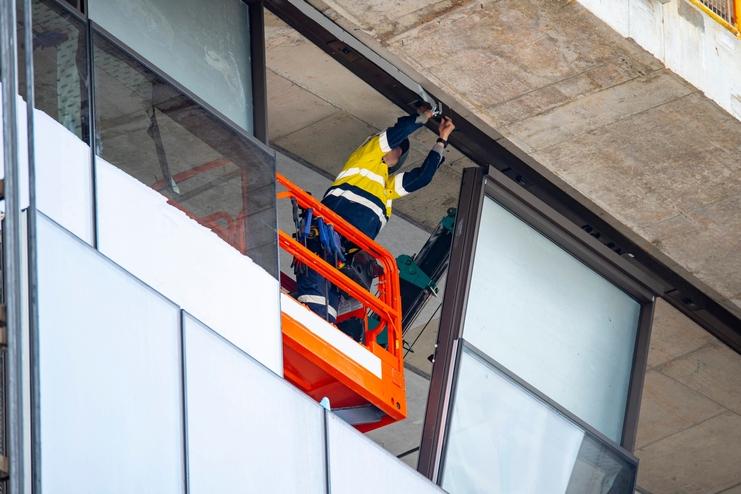 Bauarbeiter in Schutzkleidung arbeitet an einer Gebäudefassade mit einem orangefarbenen Hebelift.